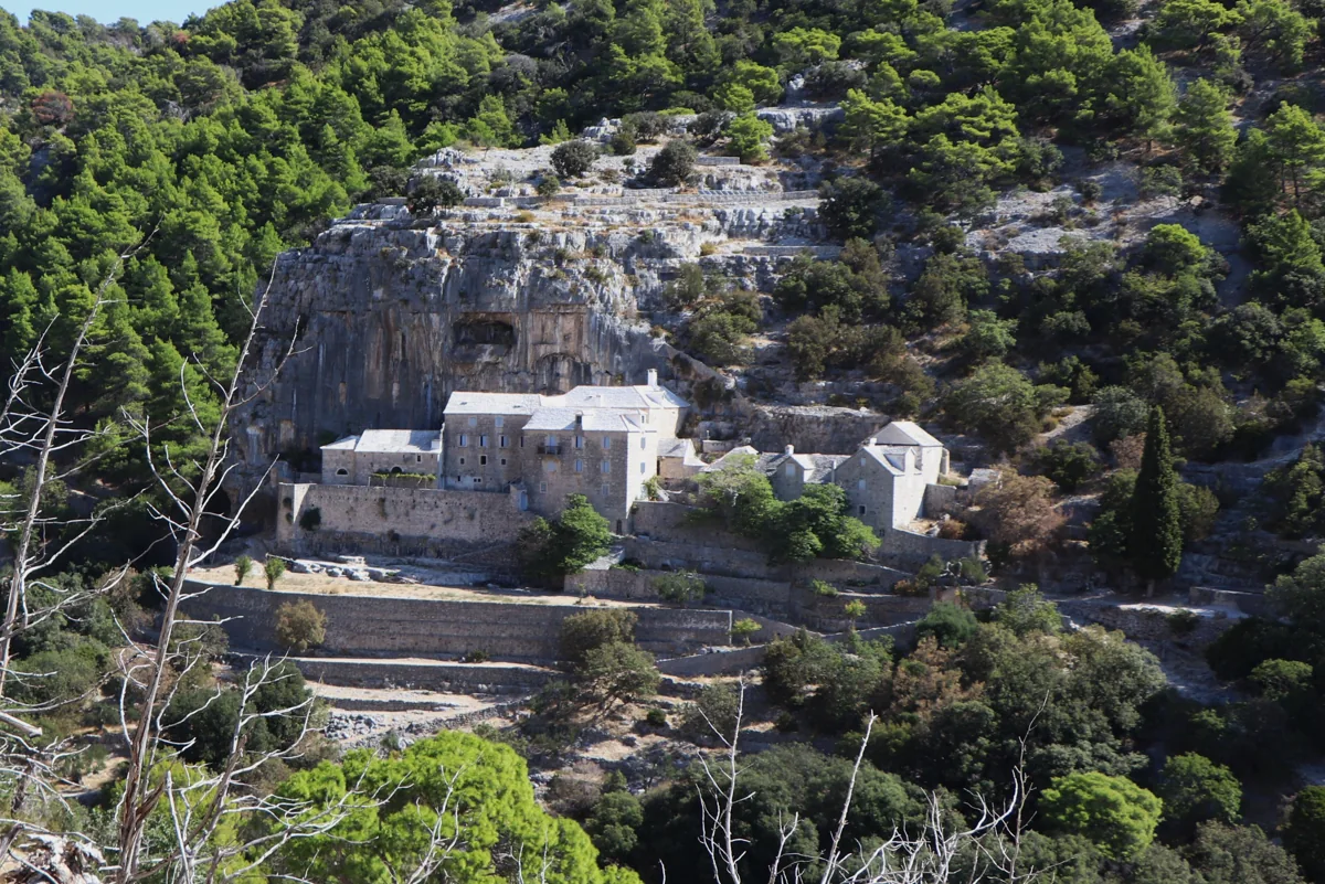 The stone buildings of Blaca Hermitage beneath a limestone cliff on Brač